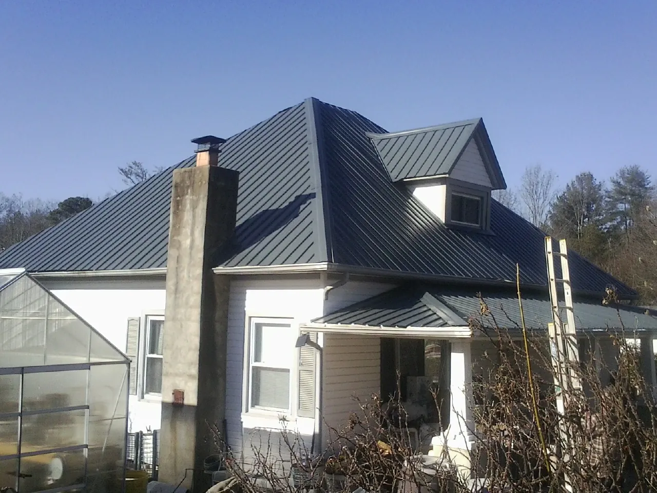 Dark blue standing seam metal roof on a white farmhouse with dormer — Slate & Tile Roof Repair by Roofing Brothers in Kyles Ford
