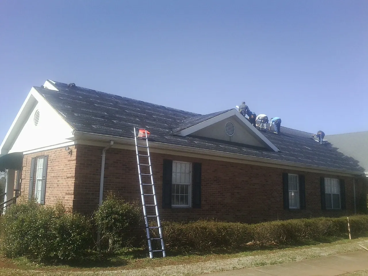 Crew tearing shingles off a brick ranch roof with a ladder set — Metal Roof Repair work by our crew in Kyles Ford