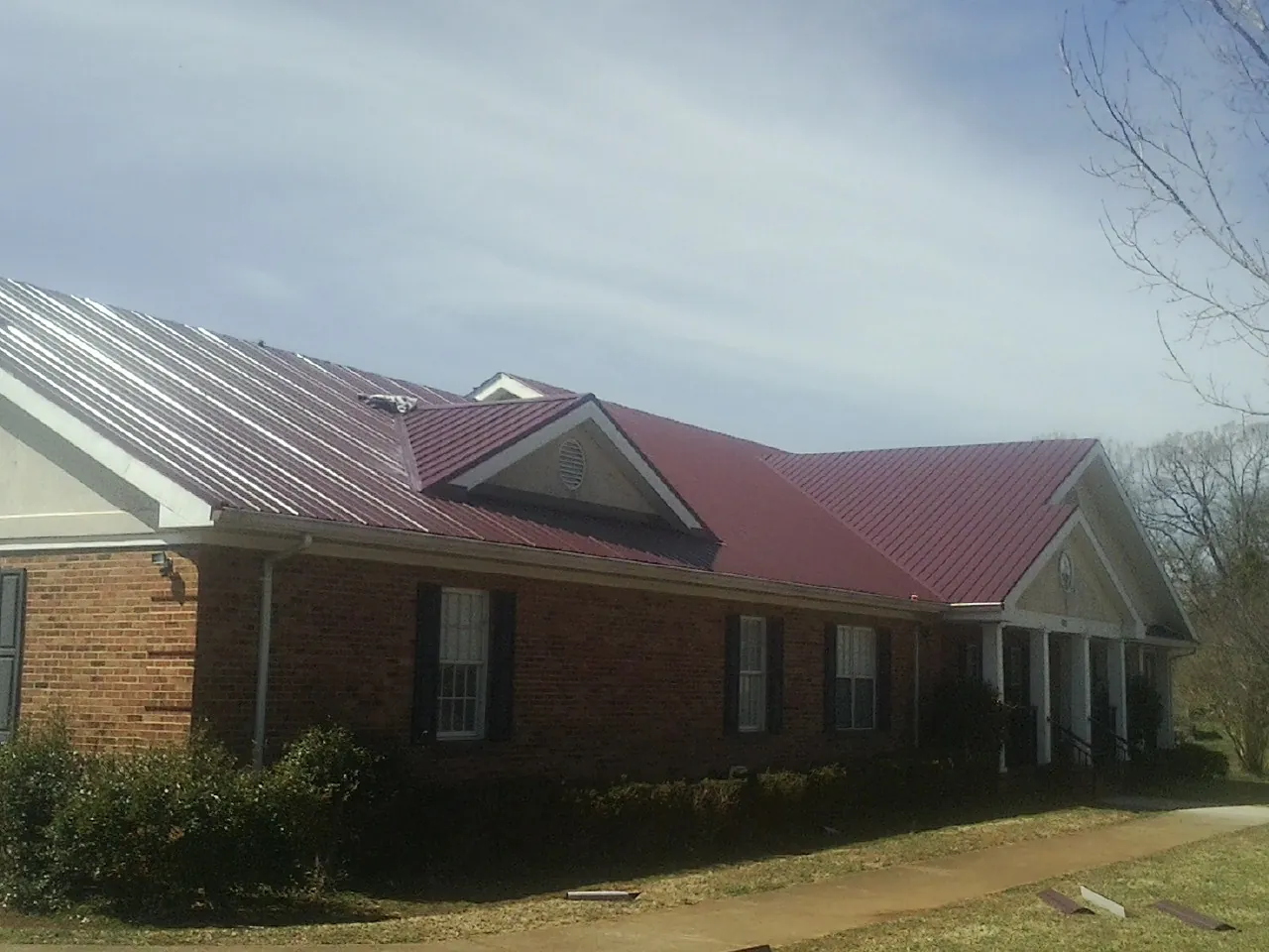 Red metal roof with gabled entries on a long brick building, from a Hail Damage Roof Repair job in Kyles Ford