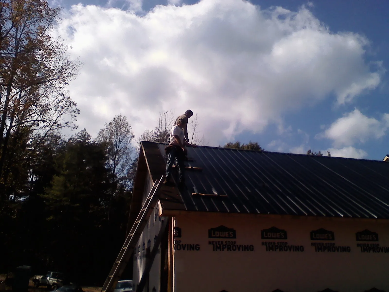 Roofer fastening dark metal panels high against a cloudy sky, from a Roof Inspection job in Kyles Ford