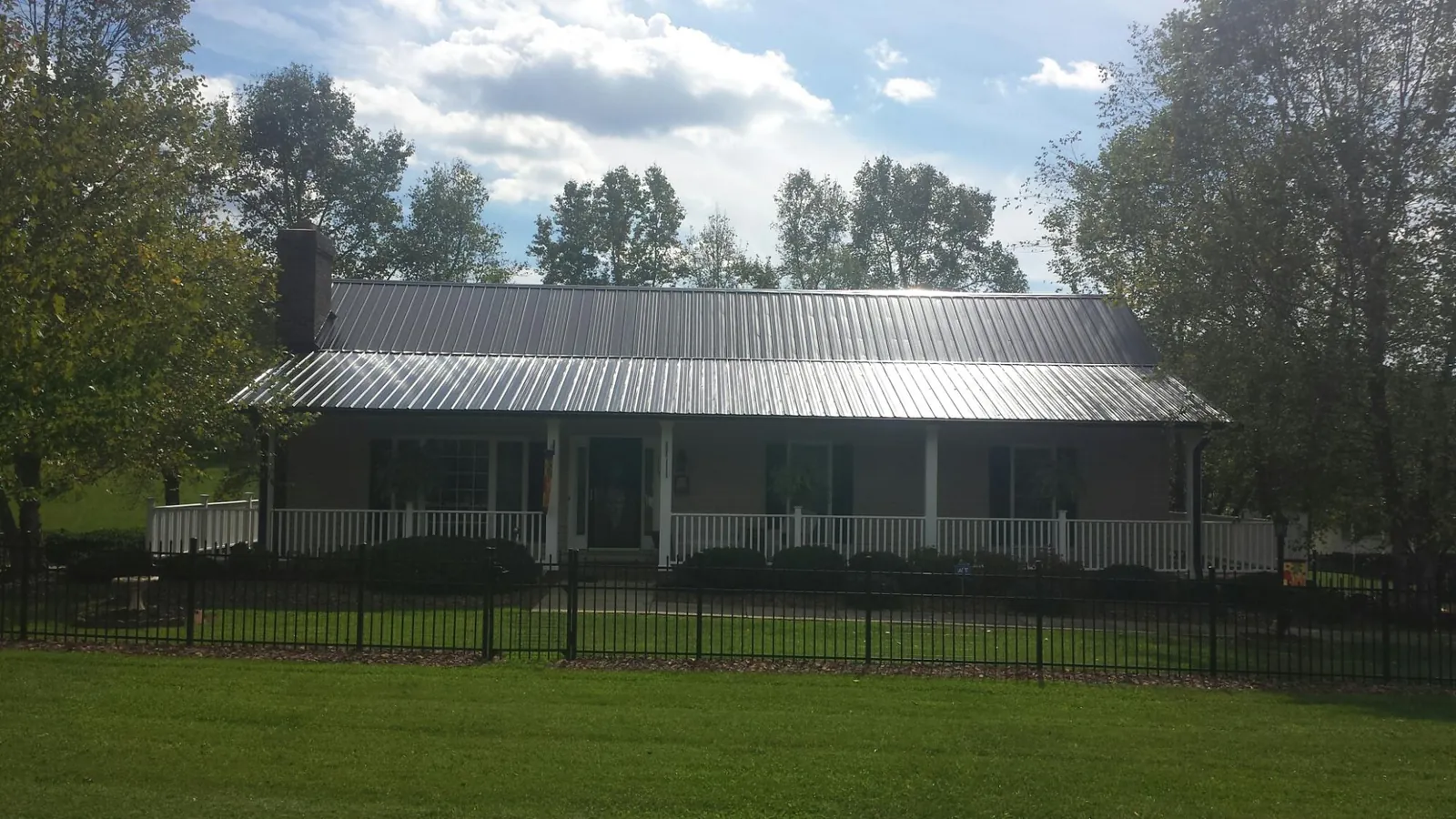 Gray metal roof on a brick ranch with a full width front porch — Gutter Guard Installation work by our crew in Kyles Ford