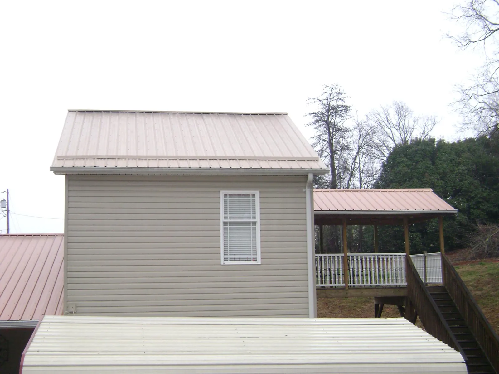 Tan metal roofs on a two story addition and attached porch, from a Roof Replacement job in Kyles Ford